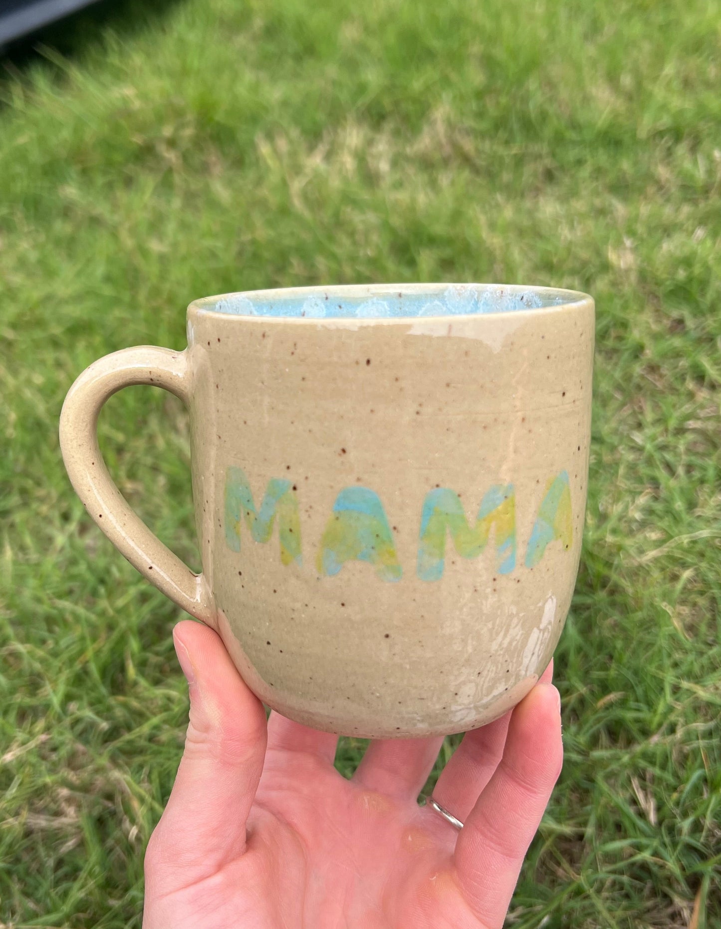 Hand holding a ceramic mug with text on a grassy background